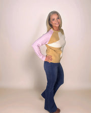 a blonde woman is standing sideways facing towards the camera with her hand on her hip and is wearing dark denim and a camel and pink colorblock sweater with a cream star on the front.