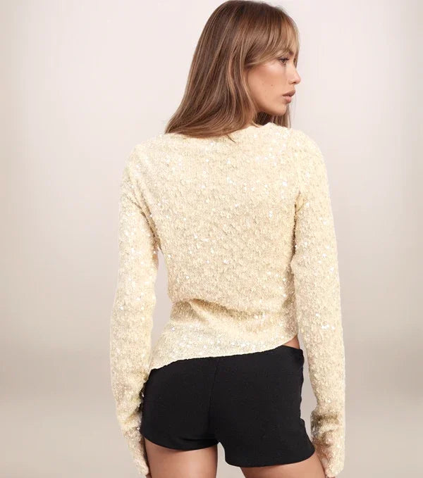 Woman wearing a textured beige sweater and black shorts on a plain background