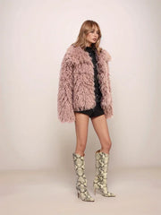 Woman wearing a fluffy pink coat and patterned high-heeled boots on a plain background