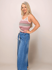Woman wearing a patterned tank top and blue jeans against a plain background