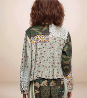 Person wearing a jacket with floral and camouflage patterns on a plain background