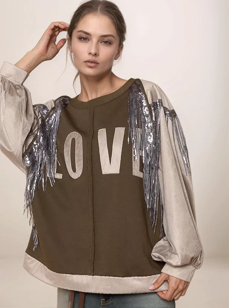 Woman wearing a brown sweatshirt with 'LOVE' and fringe details on a beige background