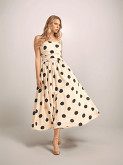 a blonde woman is wearing a cream colored dress with black polka dots. It has a full skirt, ruched bodice and spaghetti straps.