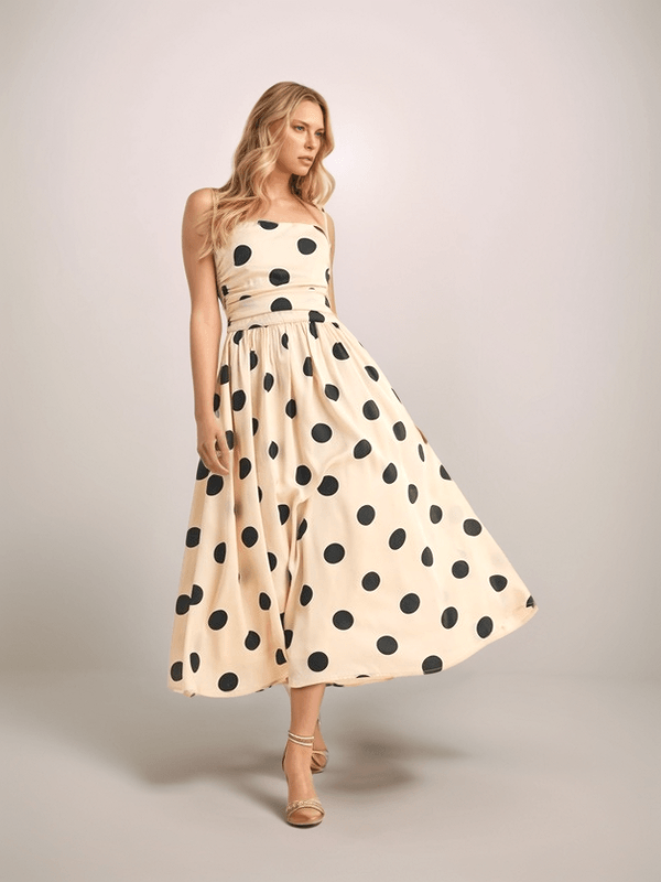 a blonde woman is wearing a cream colored dress with black polka dots. It has a full skirt, ruched bodice and spaghetti straps.