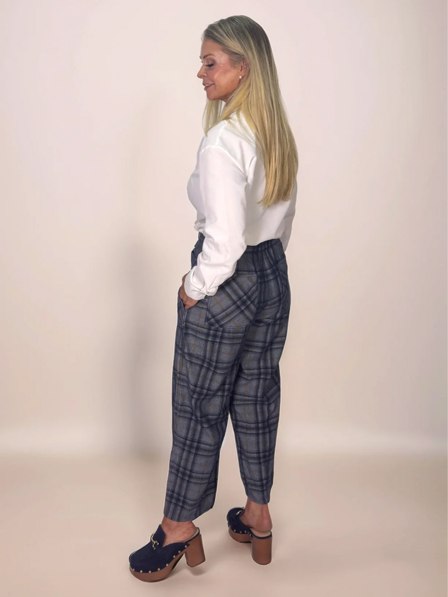 Woman wearing a white shirt and blue plaid pants against a beige background