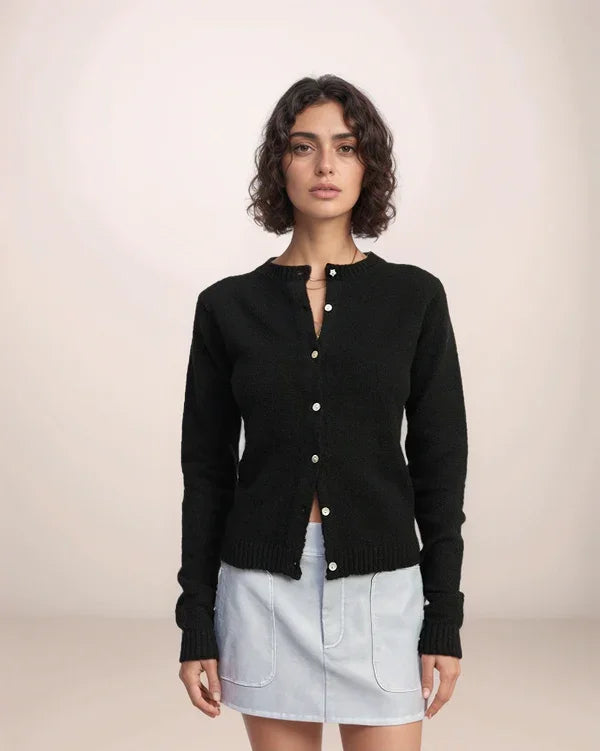 Woman wearing a black cardigan over a light blue skirt on a plain background