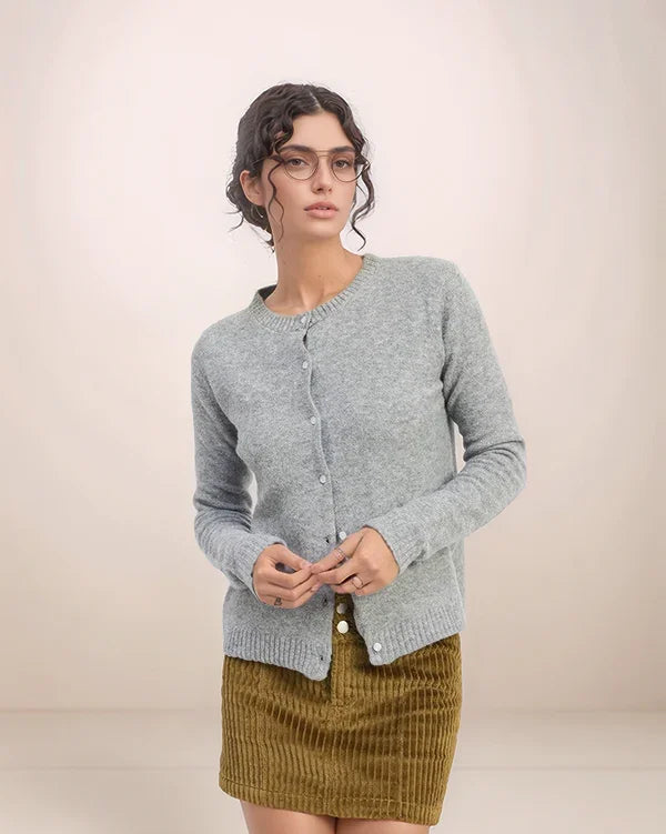 Woman wearing a gray cardigan over a green skirt against a plain background