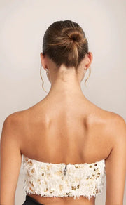 Back view of a woman wearing a strapless white lace top against a plain background