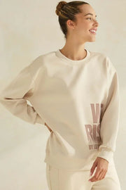 Woman wearing a beige sweatshirt with text on a plain background