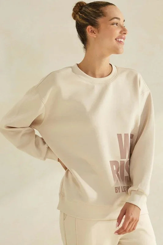 Woman wearing a beige sweatshirt with text on a plain background