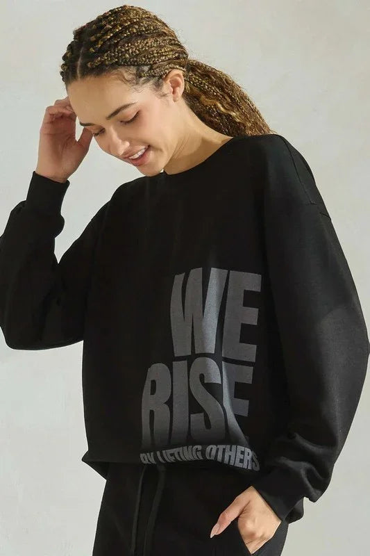 Person wearing a black sweatshirt with 'WE RISE' text on a plain background