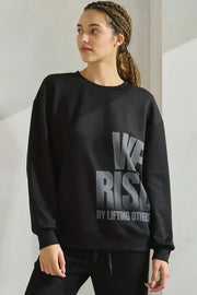 Person wearing a black sweatshirt with text, standing against a plain background