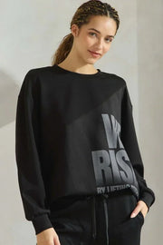 Woman wearing a black sweatshirt with 'We Rise' text on a plain background