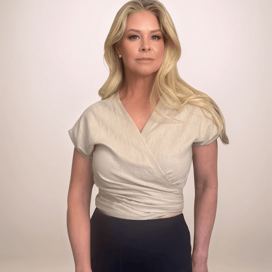 A blonde woman is wearing a beige wrap top with a v-neck and it is tied in the back.
