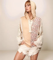 Woman wearing a stylish outfit with a beige hoodie and floral patterned top against a plain background