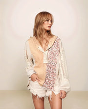 Woman wearing a floral top, beige vest, and white shorts against a plain background