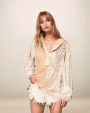 Woman wearing a beige top and white lace cover-up against a plain background