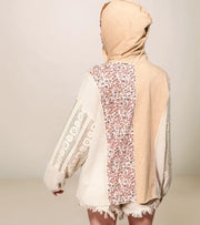 Person wearing a beige hooded garment with floral pattern on a plain background