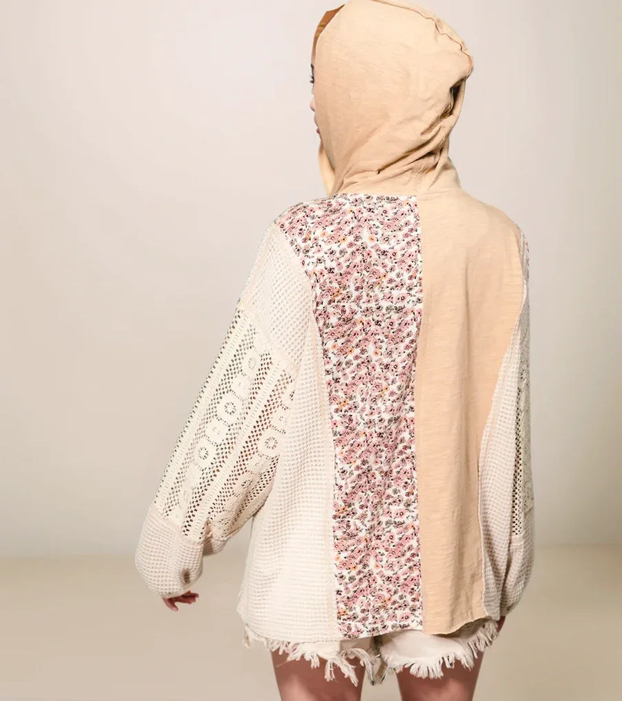 Person wearing a beige hooded garment with floral pattern on a plain background