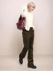 Person wearing a white sweater and olive corduroy pants holding a maroon bag against a plain background