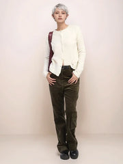 Person wearing a white cardigan, dark patterned pants, and black shoes on a plain background