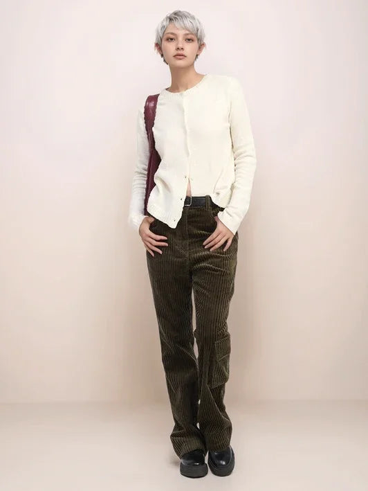 Person wearing a white cardigan, dark patterned pants, and black shoes on a plain background