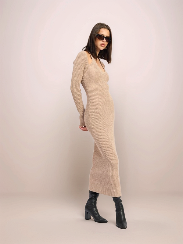 Woman wearing a beige ribbed dress and black boots against a plain background
