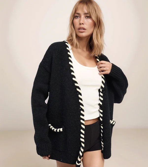 Woman wearing a black cardigan with white trim against a plain background