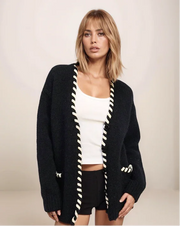 Woman wearing a black cardigan with white trim on a plain background