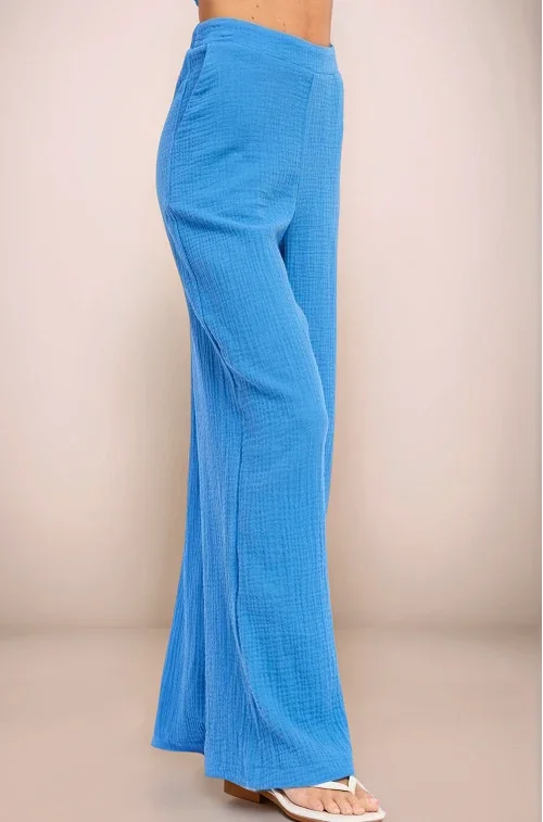A three-quarter front view of the Aegean blue wide-leg pants, highlighting the natural crinkle texture of the double gauze cotton and the spacious, flowy fit through the leg.