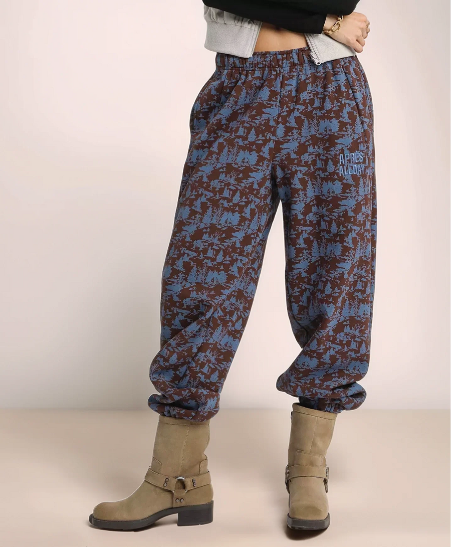 Person wearing blue and brown patterned pants with beige boots on a plain background