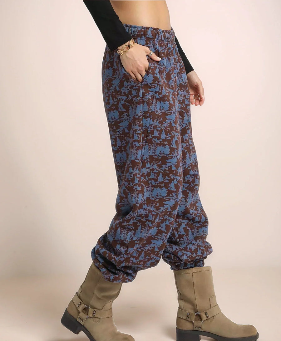 Person wearing blue patterned pants and brown boots on a beige background