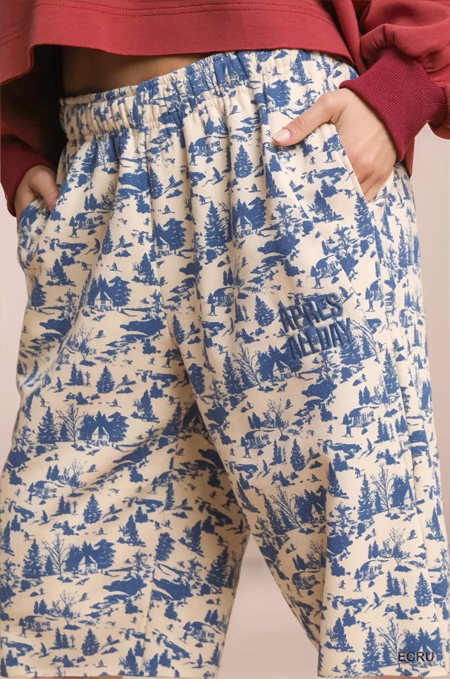 Beige pants with blue forest pattern worn by a person, on a beige background