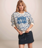 Woman wearing a patterned sweatshirt with text and a navy skirt on a plain background