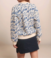 Woman wearing a blue and white patterned blouse with a beige cardigan and black skirt on a beige background