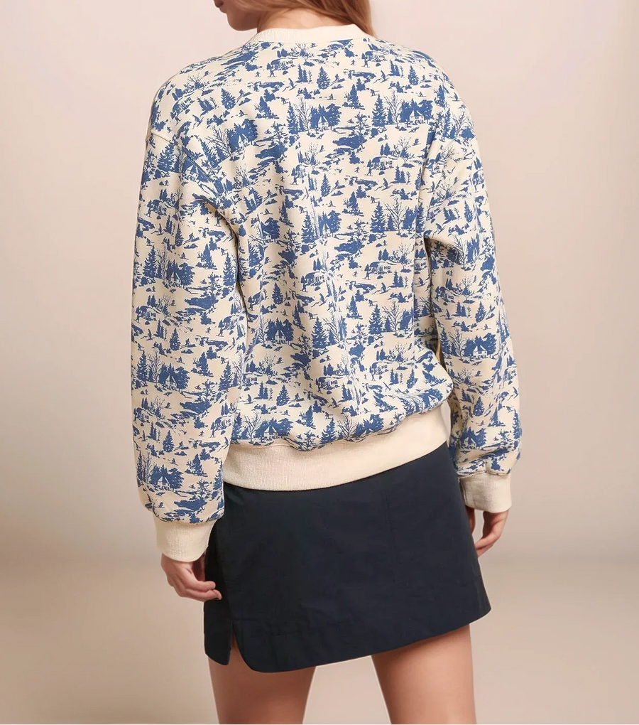 Woman wearing a blue and white patterned blouse with a beige cardigan and black skirt on a beige background