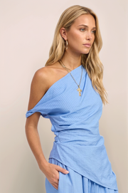 A three-quarter angled view of the Marais top in blue, capturing the sculptural movement of the asymmetrical hem and the sophisticated, one-shoulder structure.