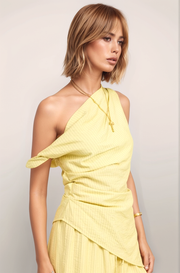 A three-quarter angled view of the Marais top in butter yellow, capturing the sculptural movement of the asymmetrical hem and the sophisticated, one-shoulder structure.