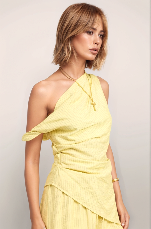 A three-quarter angled view of the Marais top in butter yellow, capturing the sculptural movement of the asymmetrical hem and the sophisticated, one-shoulder structure.