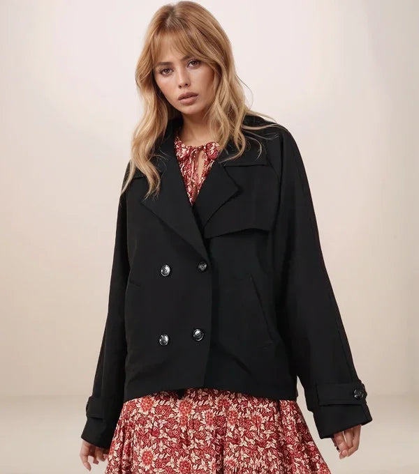 Woman wearing a black cropped trench coat over a floral dress on a plain background
