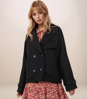 Woman wearing a black cropped trench coat over a floral dress on a plain background