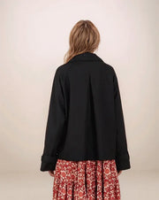 Person wearing a black jacket over a red floral dress on a plain background