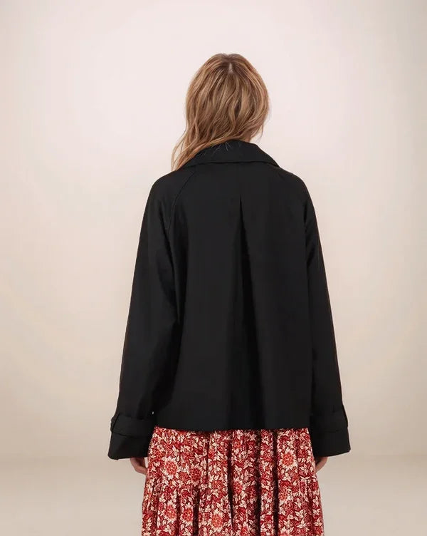 Person wearing a black jacket over a red floral dress on a plain background