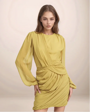 Woman wearing a yellow dress with long sleeves against a plain background