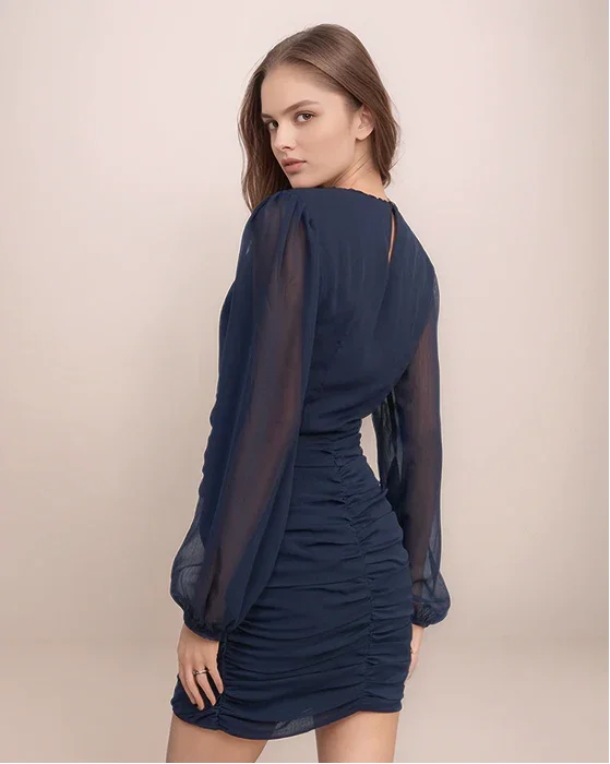 Woman wearing a navy blue dress with sheer sleeves on a beige background