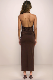 A full-length back view of the Aurelia set in espresso brown, featuring the dramatic architectural open-back halter top and the coordinating smoothing maxi skirt. The high-stretch nylon-spandex blend provides a sleek, body-con silhouette that flows into a maxi hem for a sophisticated evening look.