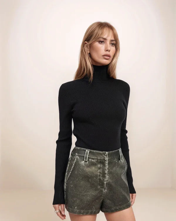 Woman wearing a black turtleneck and high-waisted denim shorts against a plain background