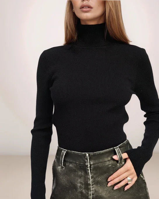 Person wearing a black turtleneck sweater and dark jeans against a plain background