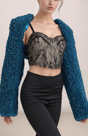 Person wearing a teal fuzzy cardigan over a black lace top and black pants on a beige background