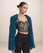 Woman wearing a blue textured cardigan over a black lace top and black pants on a beige background